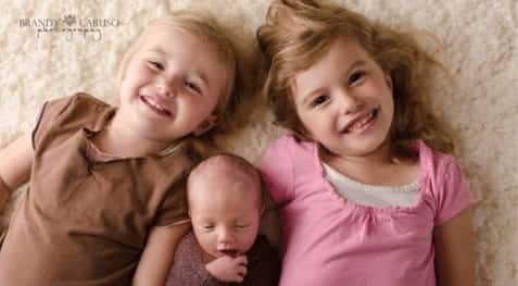 three siblings - two small smiling children and an infant